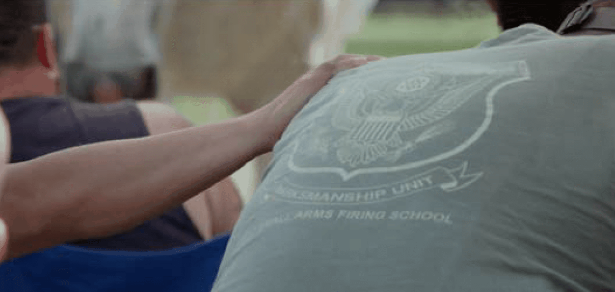 At a Veteran Retreats Foundation retreat, a veteran rests his hand on the back of a fellow veteran in a green shirt